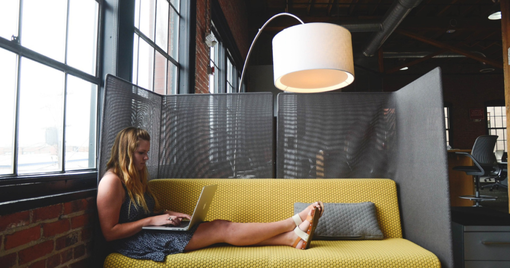 blonde freelancer comfortably sitting on a yellow sofa while working on a freelancing project.