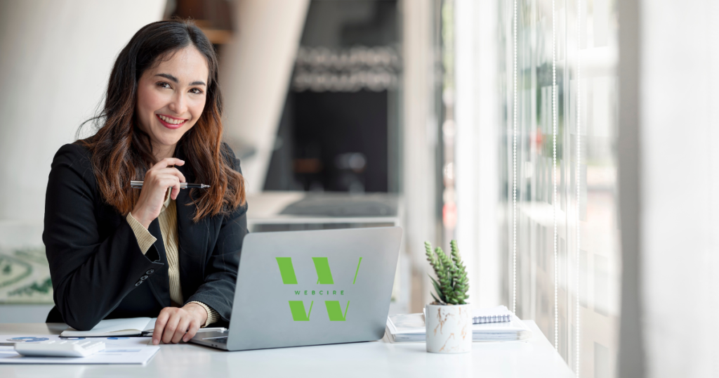 lady in corporate clothes smiling facing a laptop on the table